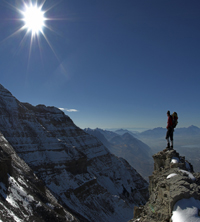 man reaching for open blue sky while standing on a high icy peak